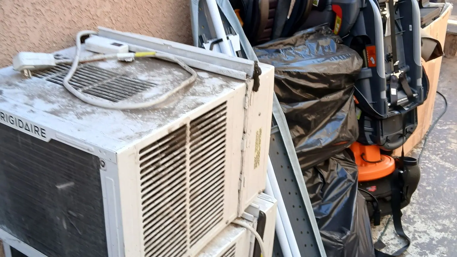 Old window air conditioners; a bike and household junk stacked for pickup