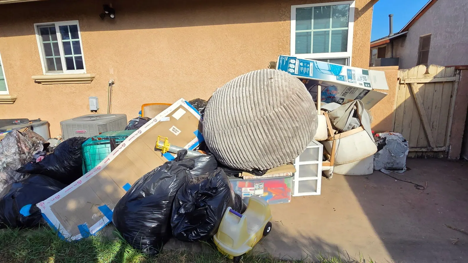Backyard pile of bagged trash; a large cushion chair and household items ready for pickup