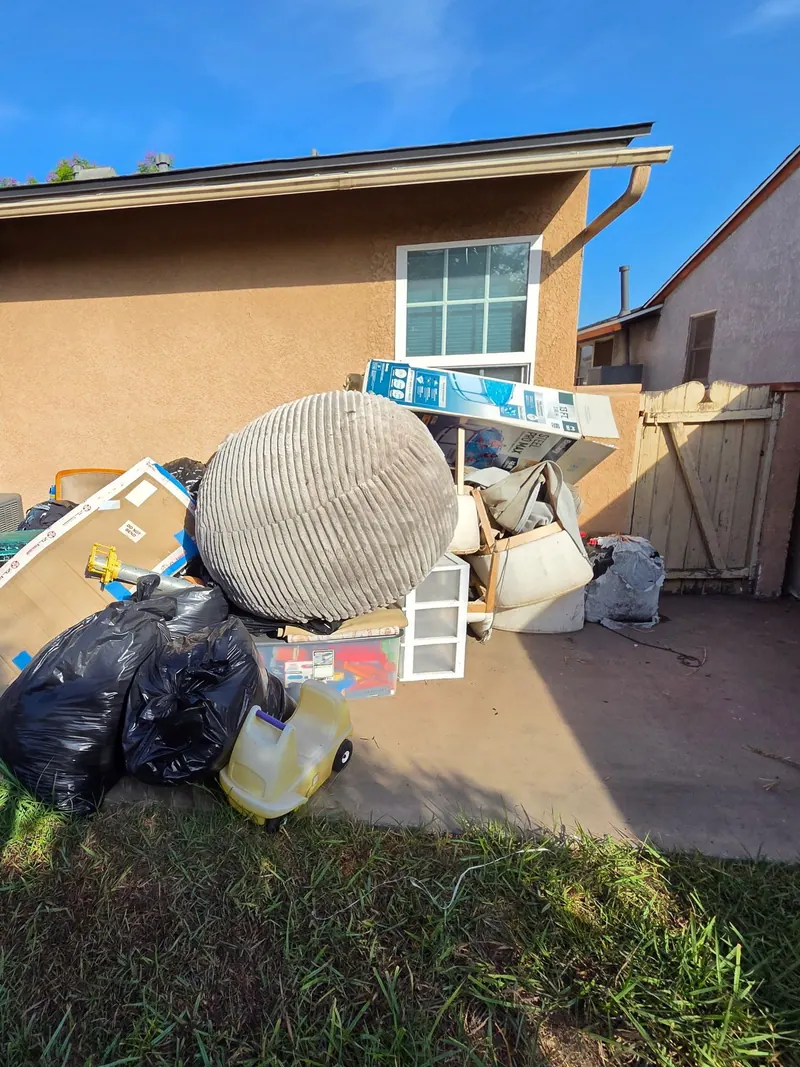 Backyard pile of bagged trash; a large cushion chair and household items ready for pickup