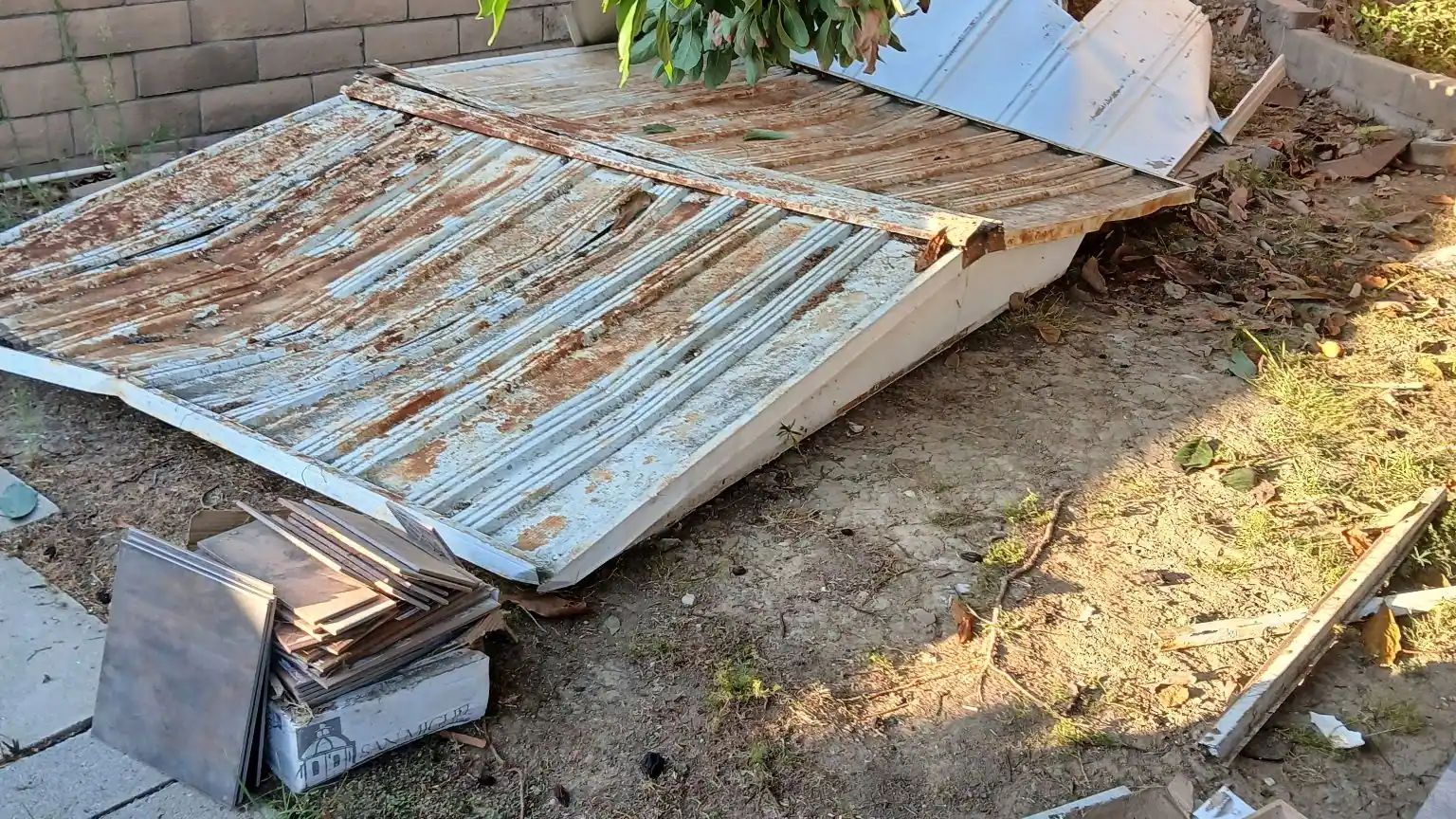 Corrugated metal panels from a taken-down shed stacked under a tree for hauling