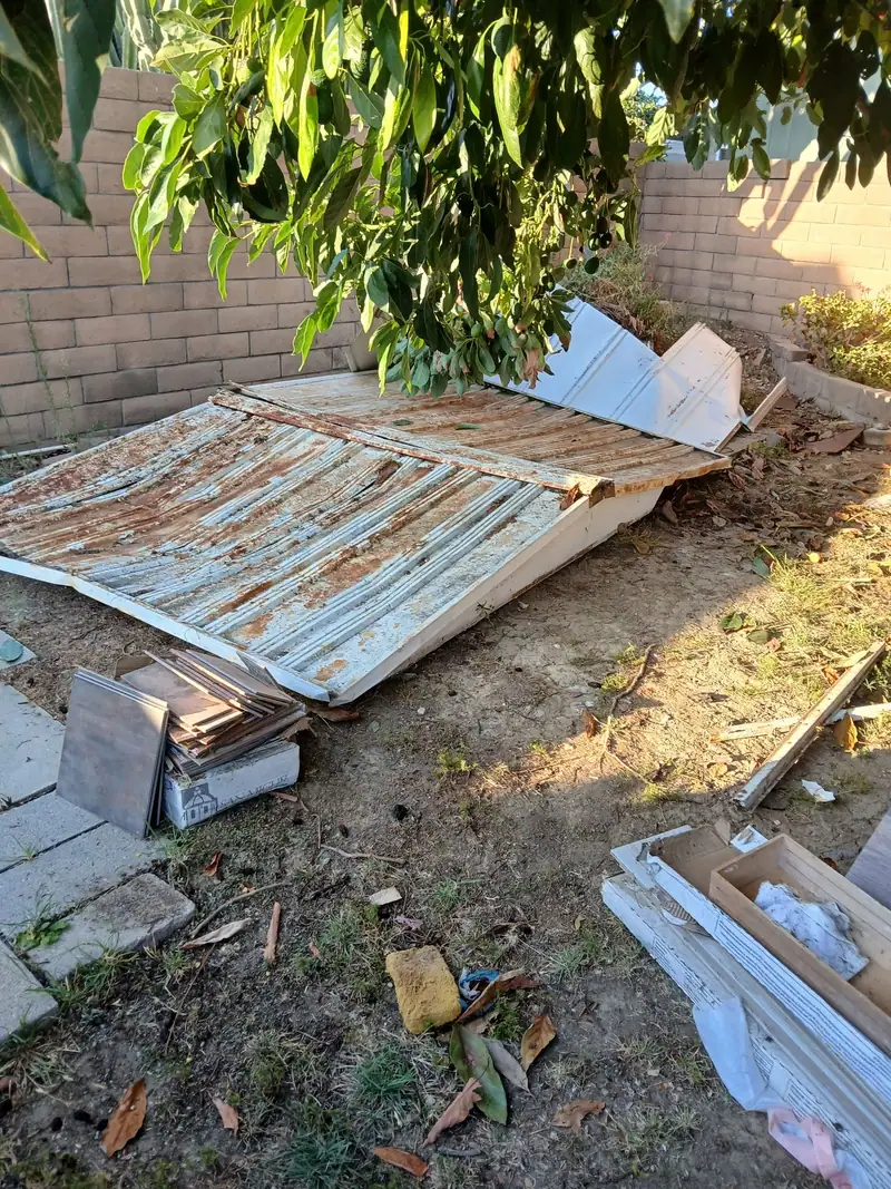 Corrugated metal panels from a taken-down shed stacked under a tree for hauling