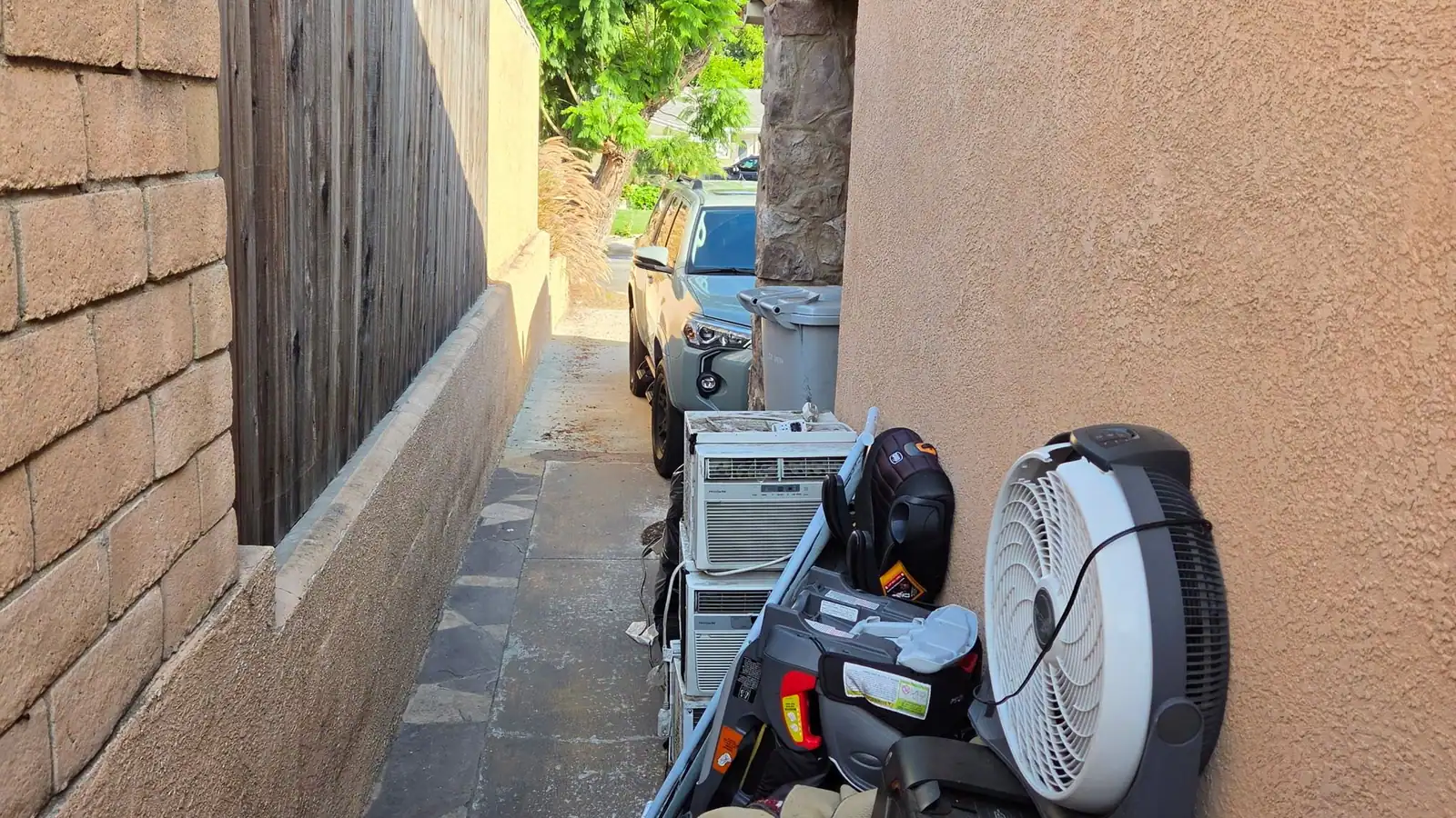 Side yard of a house lined with old fans; an air conditioner and junk waiting to be hauled
