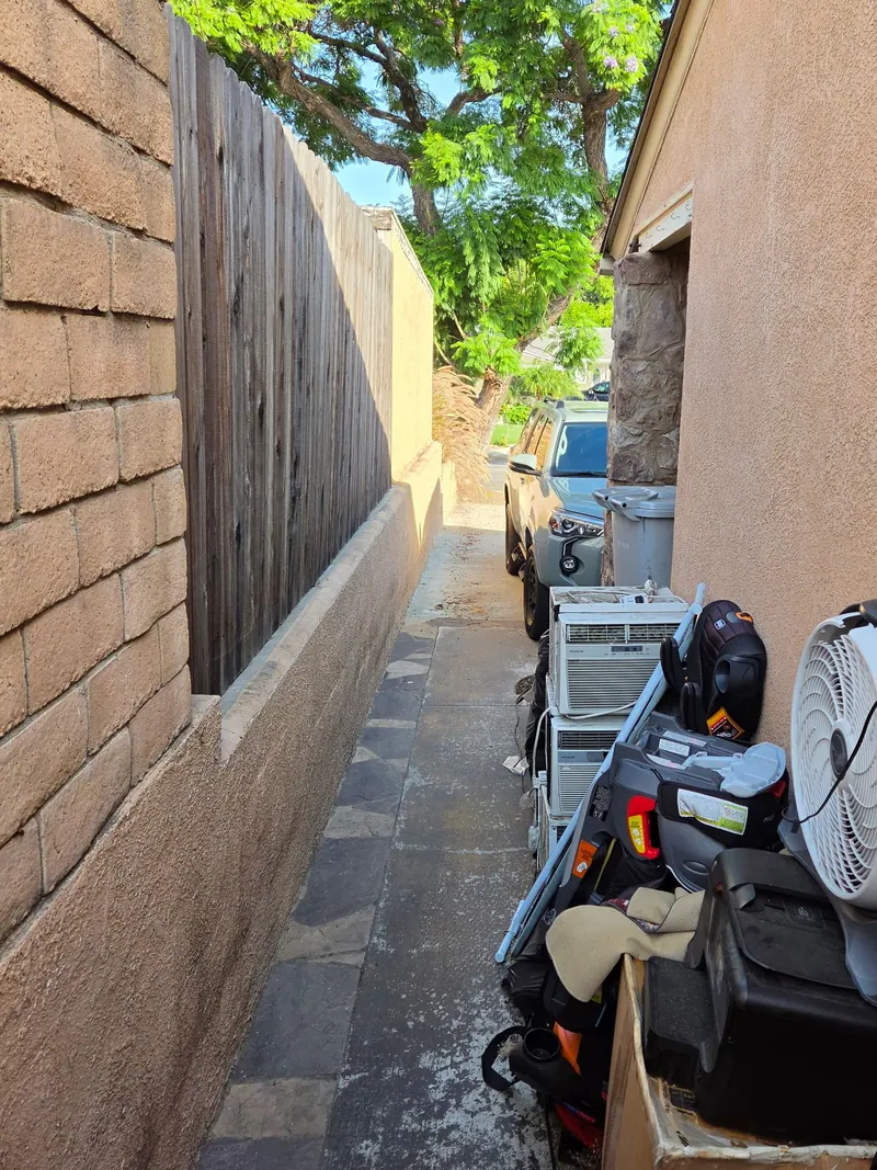 Side yard of a house lined with old fans; an air conditioner and junk waiting to be hauled