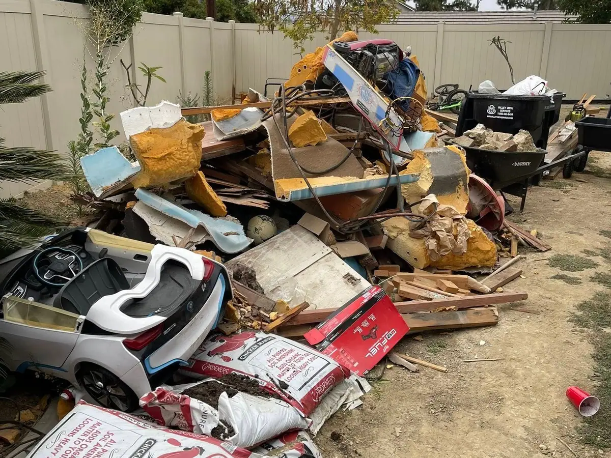 A backyard piled with broken toys; bags; wood scraps and junk against a vinyl fence