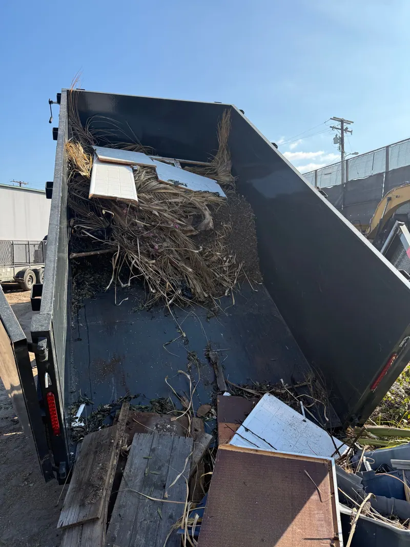 Branches and broken wood sliding out of the tipped Cast Out dump trailer